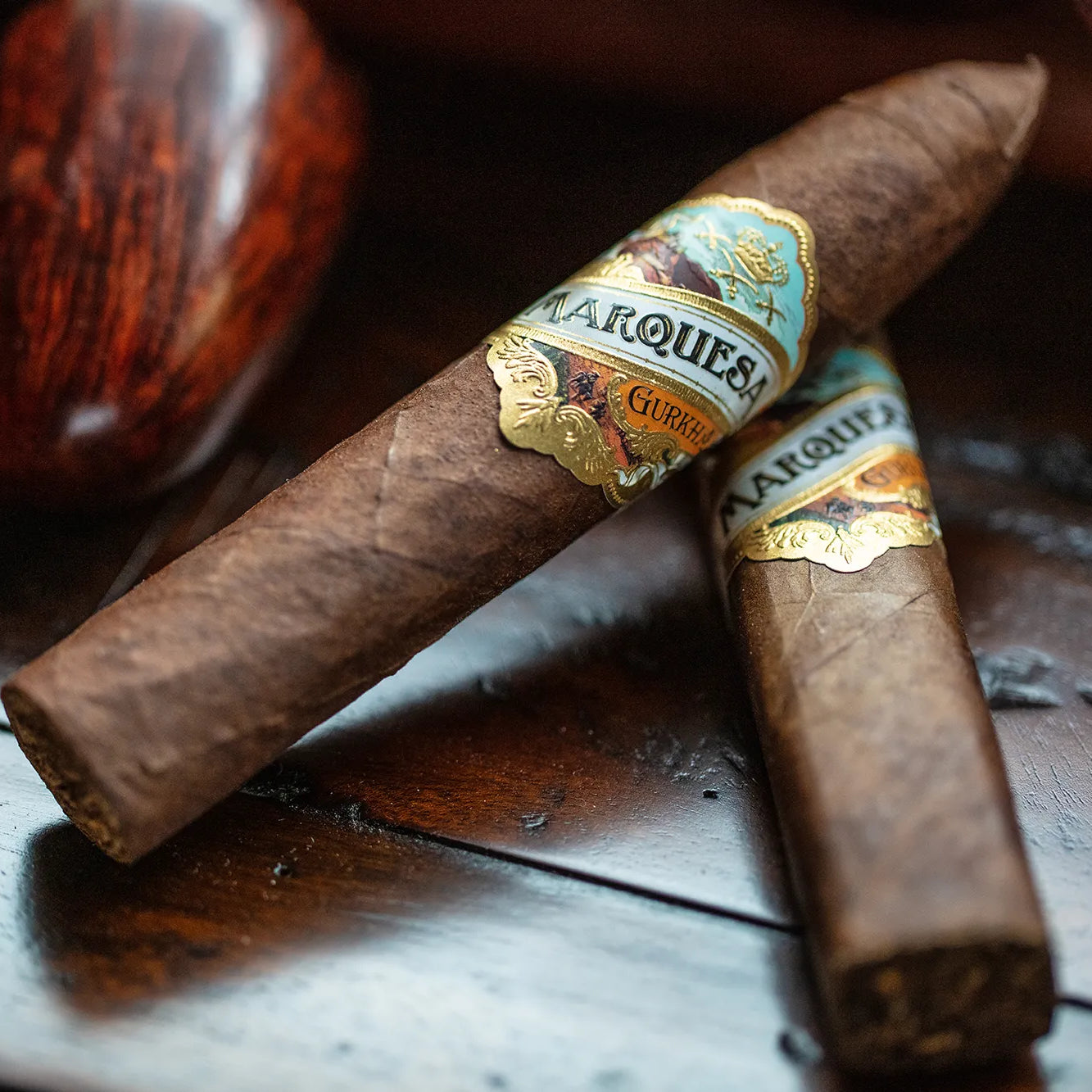 Two cigars with 'Marquis' branding on a wooden surface next to a pipe.