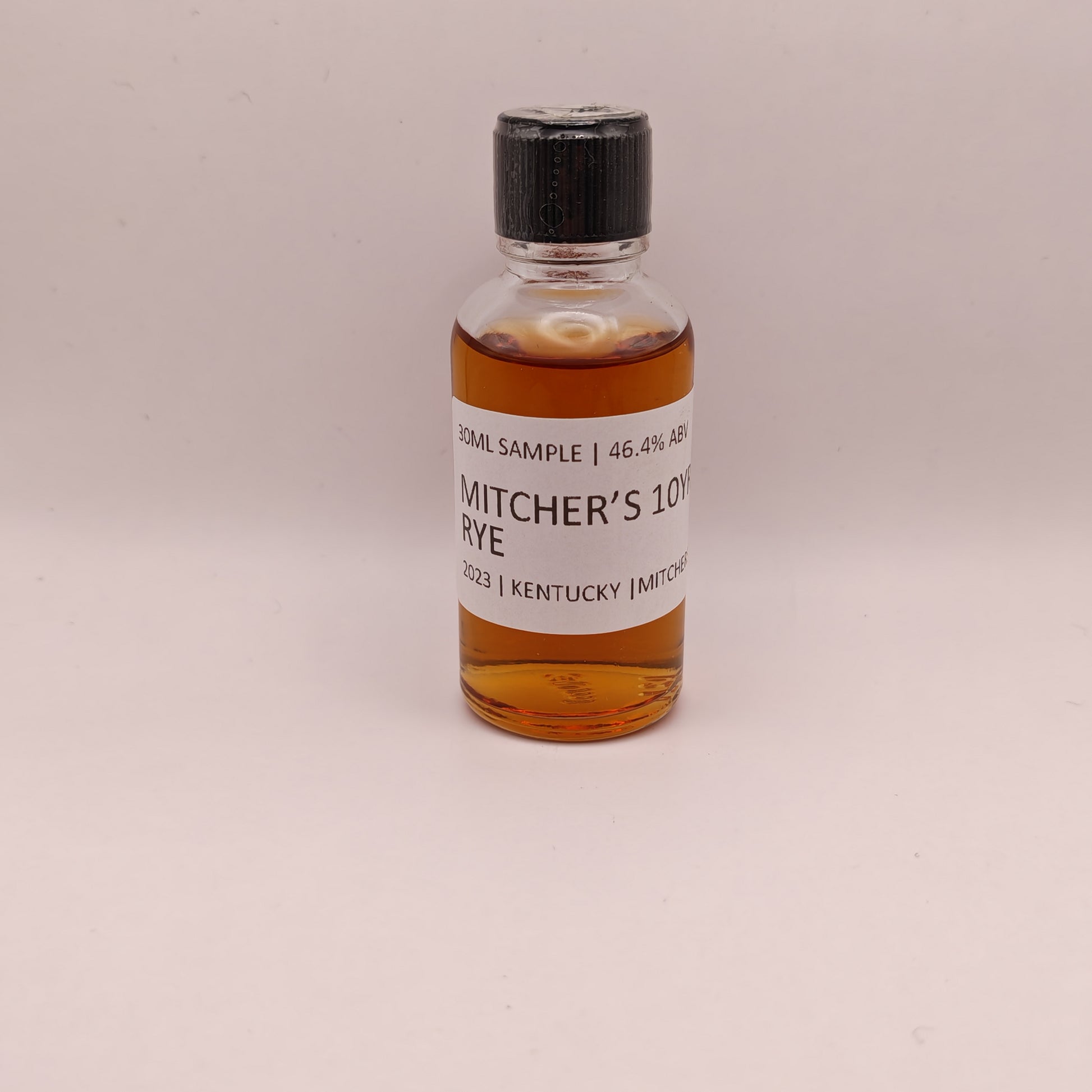 Small bottle of Mitcher's 10 Year Rye whiskey sample on a beige background