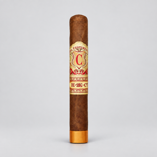 A single brown cigar standing upright on a light gray background, featuring a cream and red band with gold detailing and a gold foot.