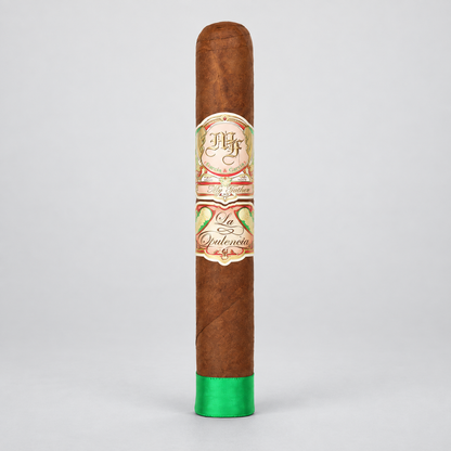 A single brown cigar standing upright on a light gray background, featuring a decorative cream and red band with green leaf illustrations and a bright green tip.
