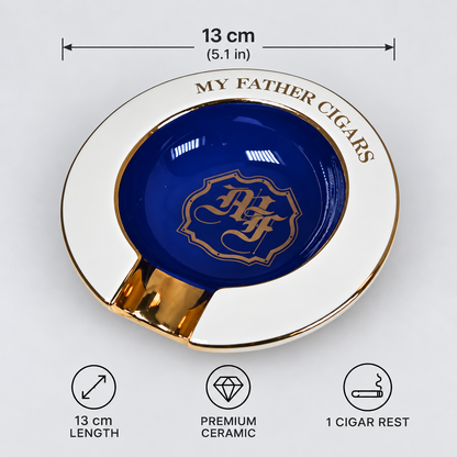 A round ceramic cigar rest with a white outer rim, gold trim, and a deep blue center featuring a gold monogram and the words 'MY FATHER CIGARS.' Measurement text above indicates 13 cm (5.