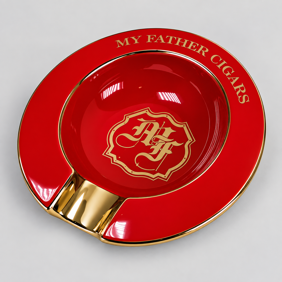 A glossy red and gold cigar ashtray with the text 'MY FATHER CIGARS' around the rim and a decorative crest in the center, photographed on a light gray background.