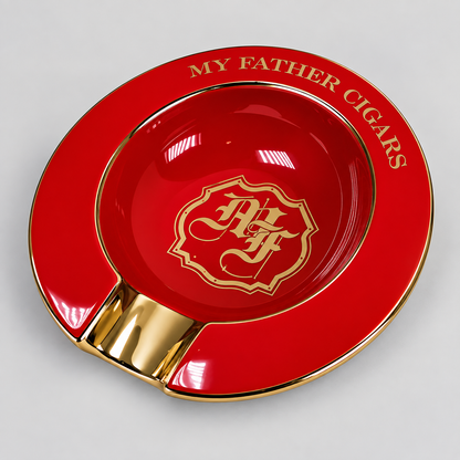 A glossy red and gold cigar ashtray with the text 'MY FATHER CIGARS' around the rim and a decorative crest in the center, photographed on a light gray background.