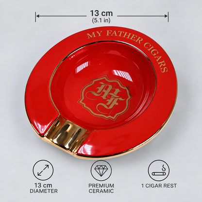 A glossy red ceramic cigar ashtray with gold trim and a gold crest emblem in the center, shown on a light gray background with dimension and feature callouts. The rim reads 'MY FATHER CIGARS'.