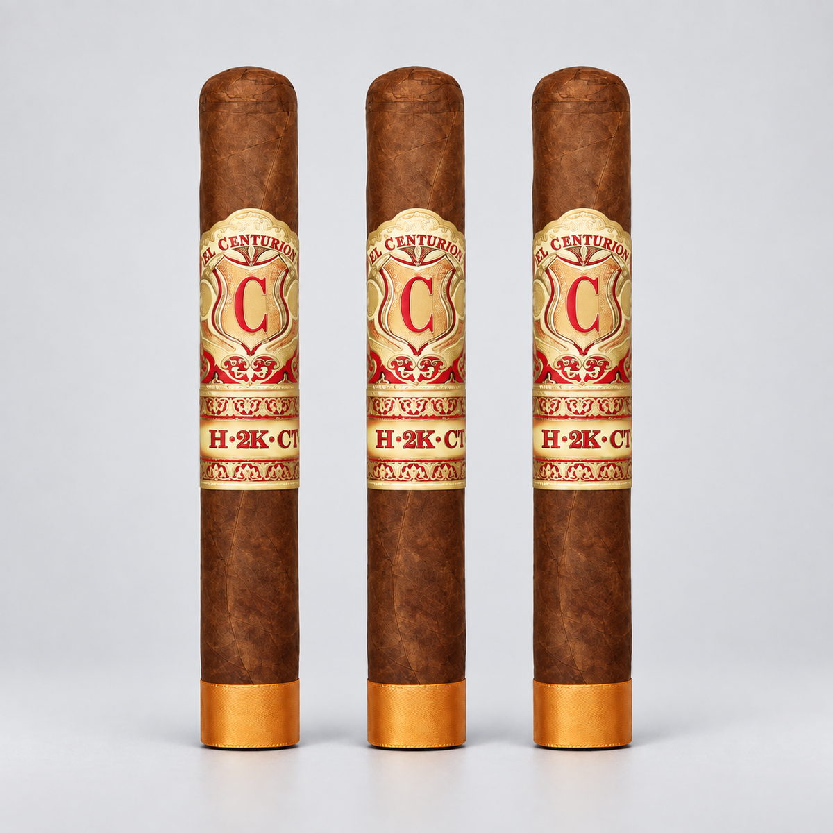 Three brown cigars standing upright on a light gray background, each with a gold and red Century Cigars H-2K-C band around the middle and gold tips at the bottom.