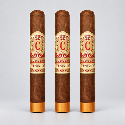 Three brown cigars standing upright on a light gray background, each with a gold and red Century Cigars H-2K-C band around the middle and gold tips at the bottom.
