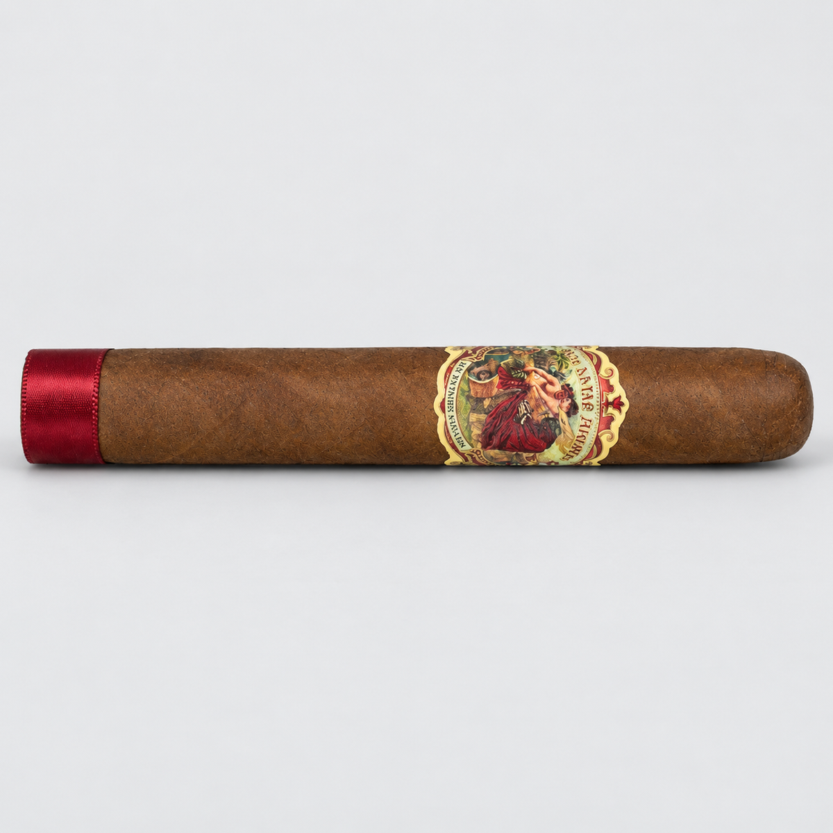 A single brown cigar with a red satin band on one end and a detailed vintage-style label in the center, photographed horizontally against a light gray background.