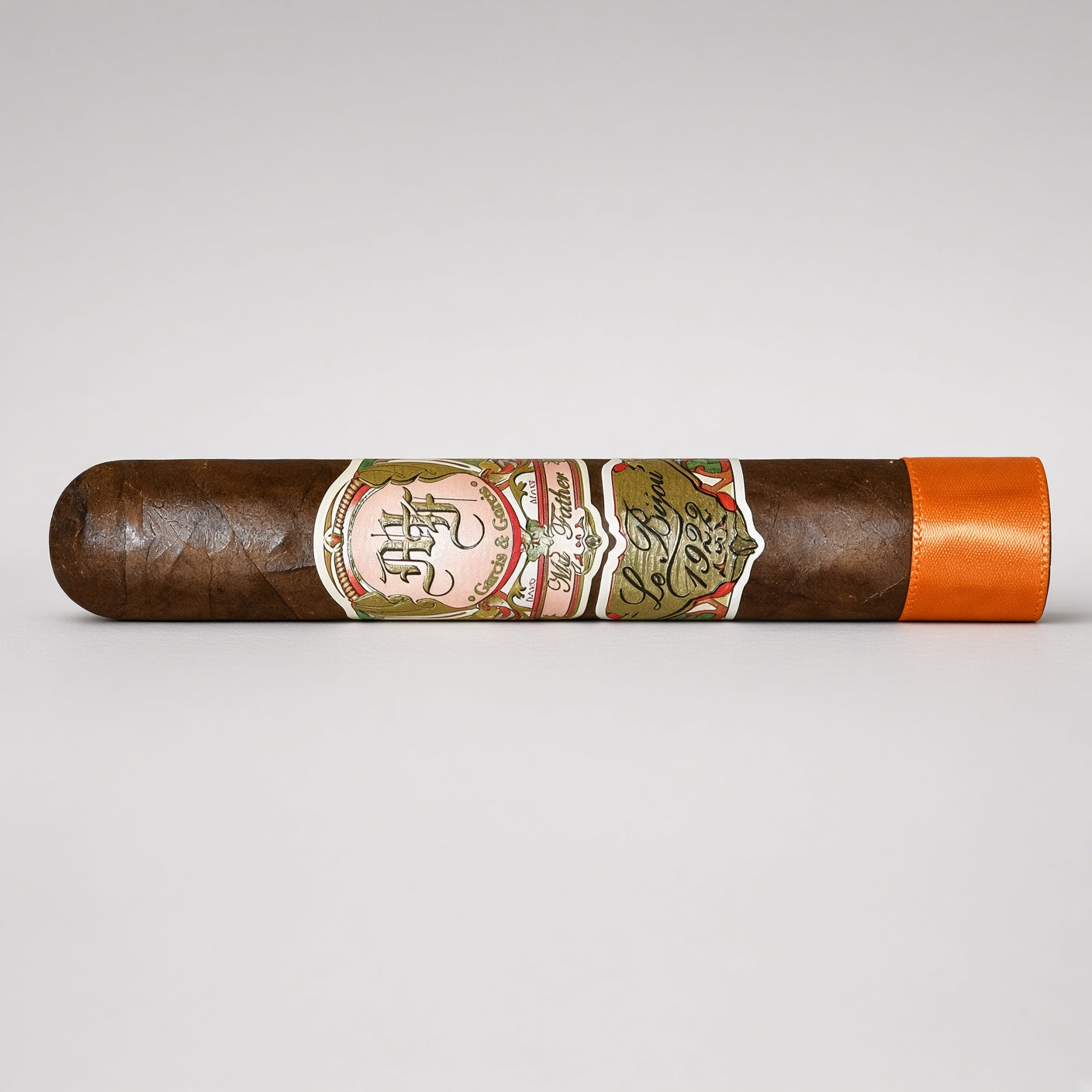 A single dark brown cigar with a detailed multicolor paper band and a bright orange tip, displayed horizontally on a light gray background.