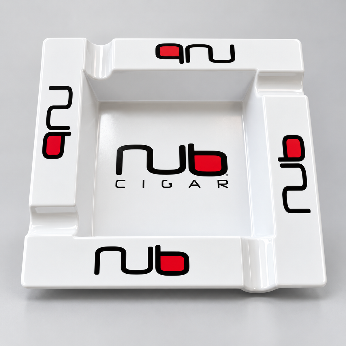 A white square ceramic cigar ashtray featuring the 'nub CIGAR' logo printed in black and red on the center and corners, set against a neutral gray background.