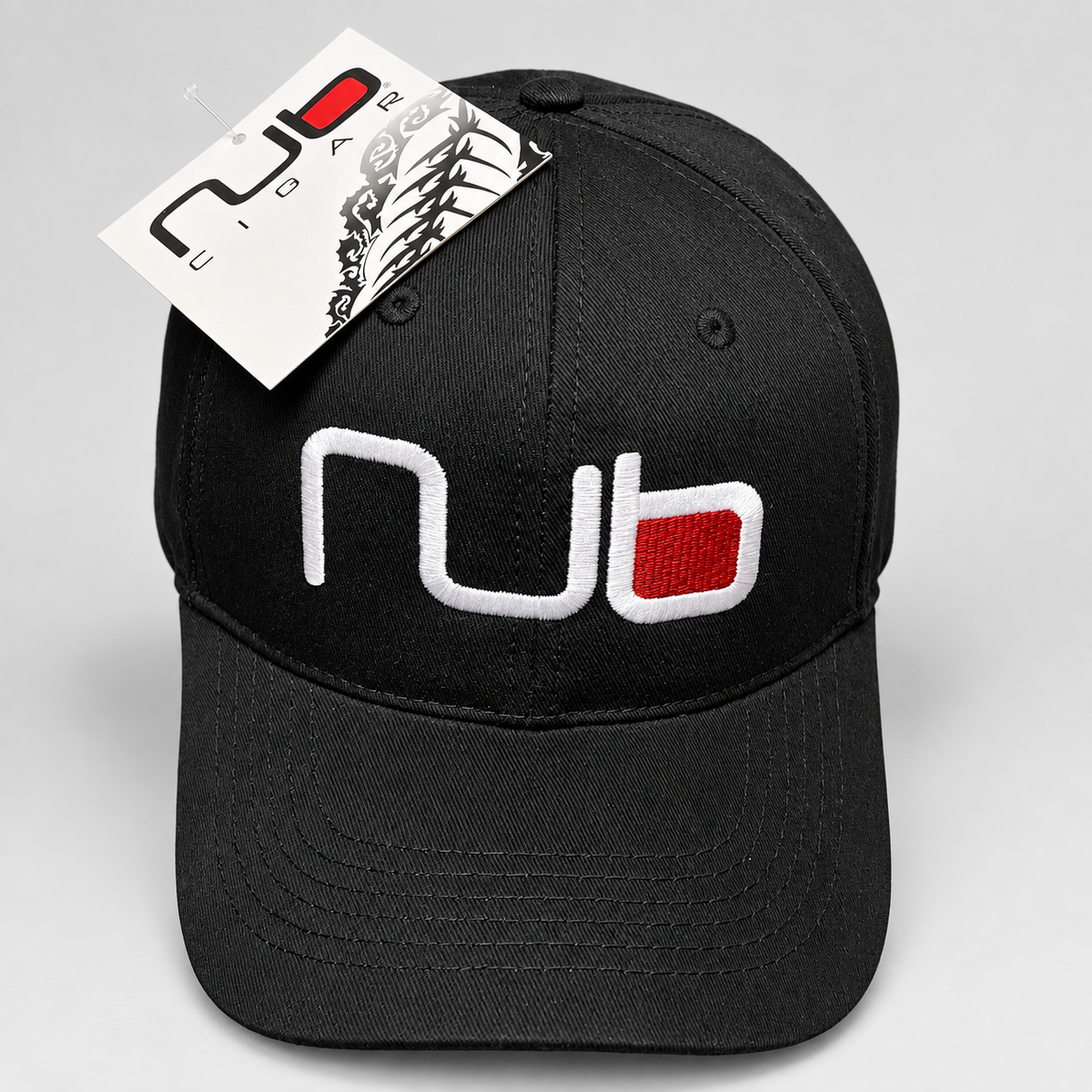 A black baseball cap with a white and red embroidered 'nub' logo on the front, featuring a white hangtag with the same logo, photographed on a light gray background.