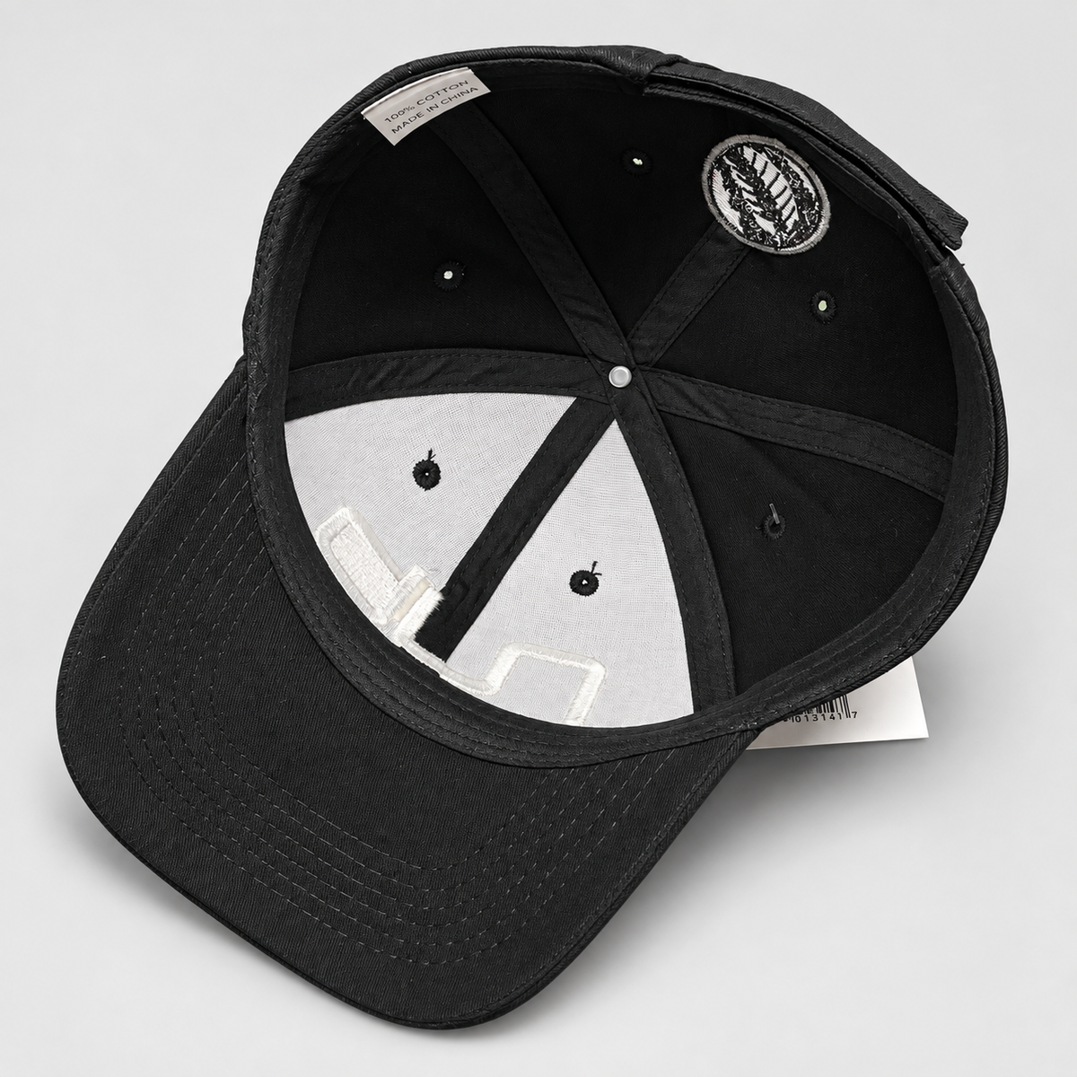 Black baseball cap shown from an overhead angle, displaying the interior crown, adjustable strap, ventilation eyelets, and a circular embroidered patch on the inside.