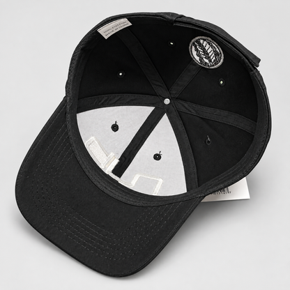 Black baseball cap shown from an overhead angle, displaying the interior crown, adjustable strap, ventilation eyelets, and a circular embroidered patch on the inside.