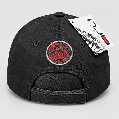 Black baseball cap with a red and black circular embroidered patch on the front, shown from the back with an adjustable strap and a white product tag attached, on a light gray background.