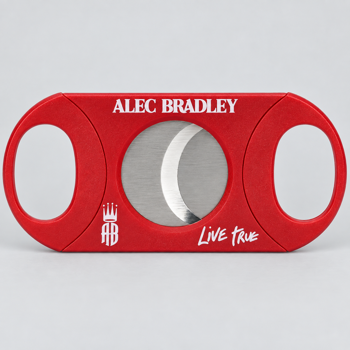 A red cigar cutter with a circular silver blade visible through the center, featuring 'ALEC BRADLEY' in white text at the top and 'Live True' with a crest logo at the bottom, set against a light gray background.