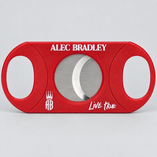 A red cigar cutter with a circular silver blade visible through the center, featuring 'ALEC BRADLEY' in white text at the top and 'Live True' with a crest logo at the bottom, set against a light gray background.
