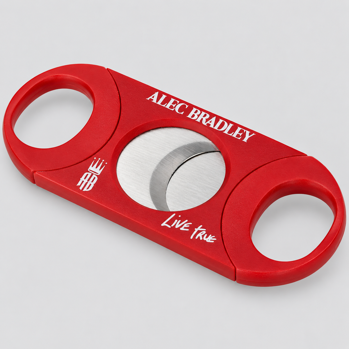 A red cigar cutter with silver stainless steel blades, featuring custom white printed text reading 'ALEC BRADLEY' and 'Live True' on a light gray background.