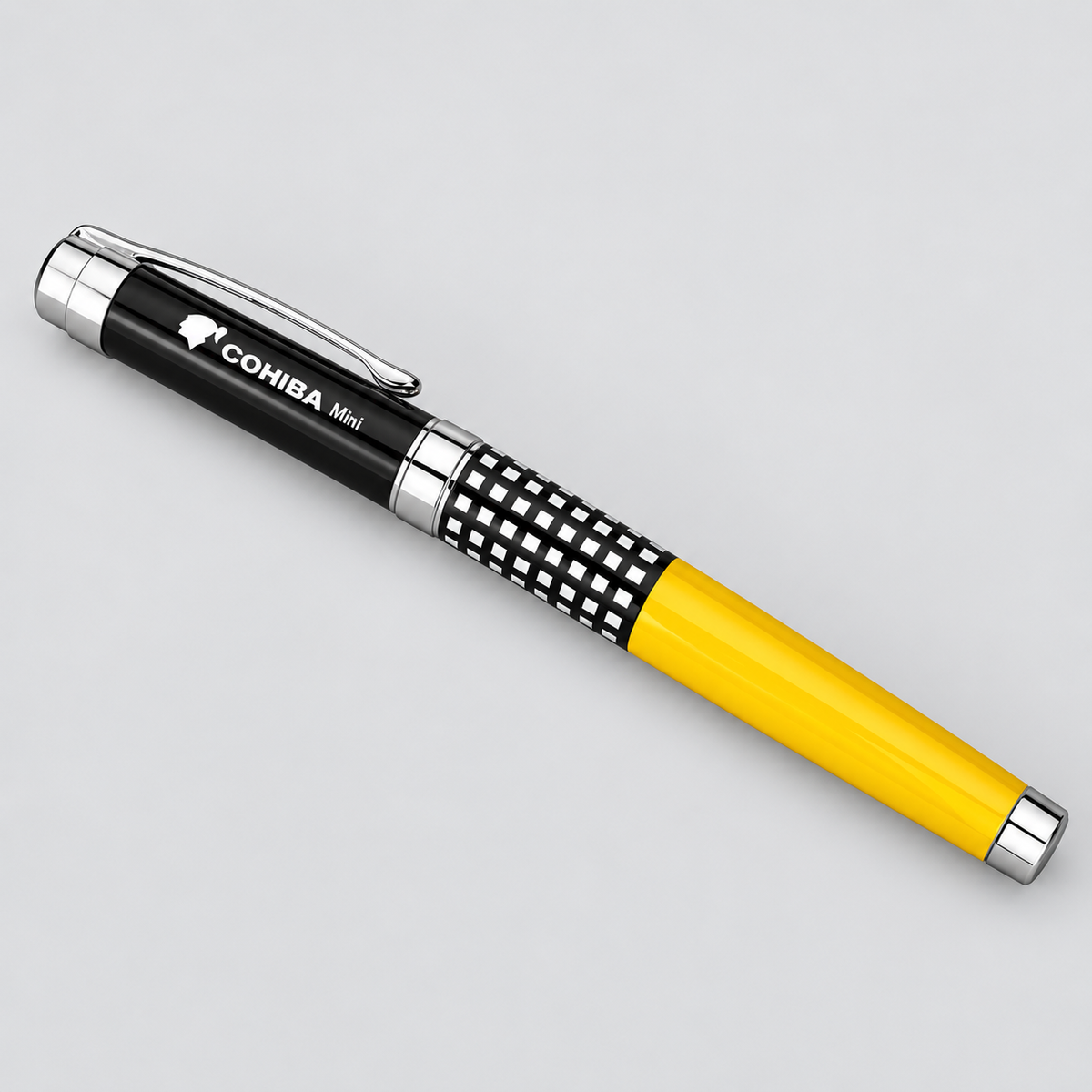 A Cohiba Mini ballpoint pen with a black and silver body, featuring a black-and-white checkered pattern and a bright yellow grip section, shown on a light gray background.