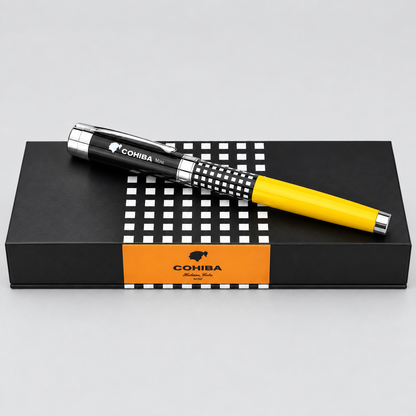 A COHIBA ballpoint pen with a black and white checkered grip and a bright yellow barrel, resting diagonally on top of its black presentation box with an orange COHIBA label.
