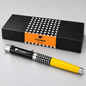 A COHIBA Mini ballpoint pen with a black and yellow body and silver accents, displayed in front of its black gift box with an orange band.