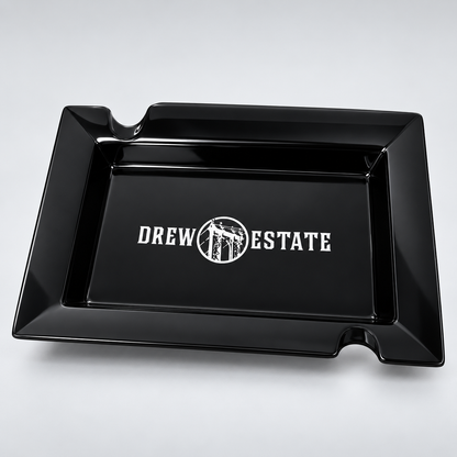 A glossy black rectangular tray with a raised rim and two small notches on the long sides, featuring the white 'DREW ESTATE' logo printed in the center, shown on a light gray background.