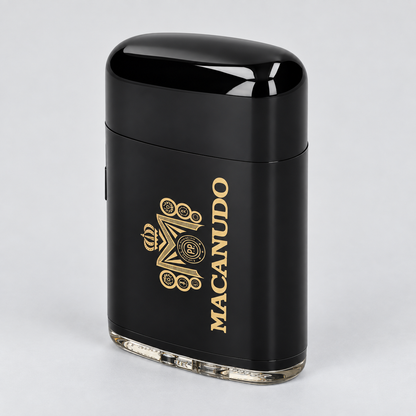 A black portable electric lighter with a glossy finish, featuring a gold 'MACANUDO' brand logo and crest on the side, set against a light gray background.