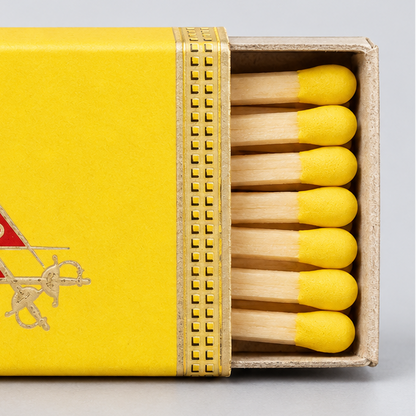 A yellow matchbox with a red and gold Monte Cristo Habana logo, shown open with wooden matches and yellow tips on a light gray background.