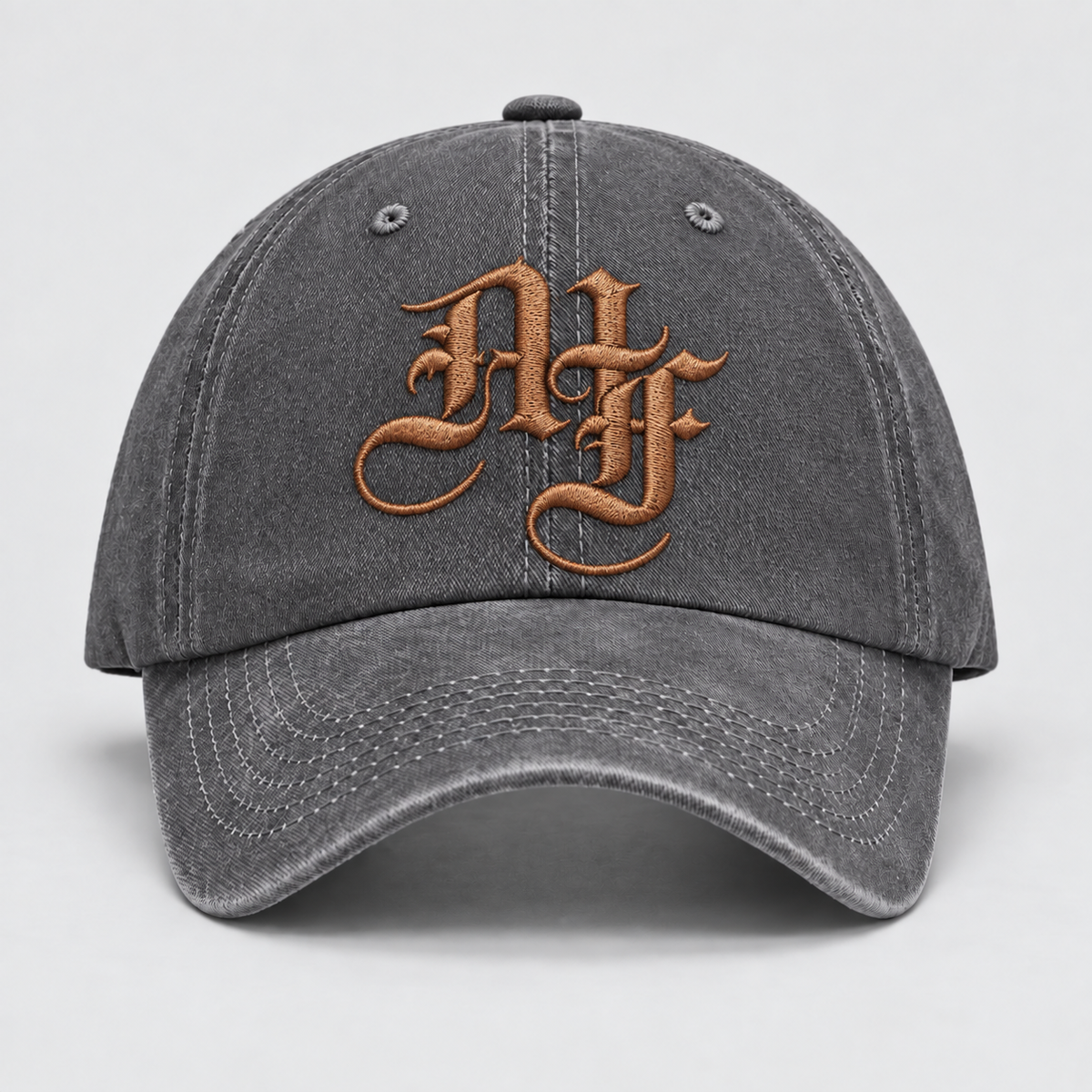 A dark gray washed cotton baseball cap featuring a prominent metallic bronze embroidered monogram logo on the front, set against a neutral light gray background.