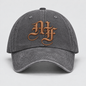A dark gray washed cotton baseball cap featuring a prominent metallic bronze embroidered monogram logo on the front, set against a neutral light gray background.