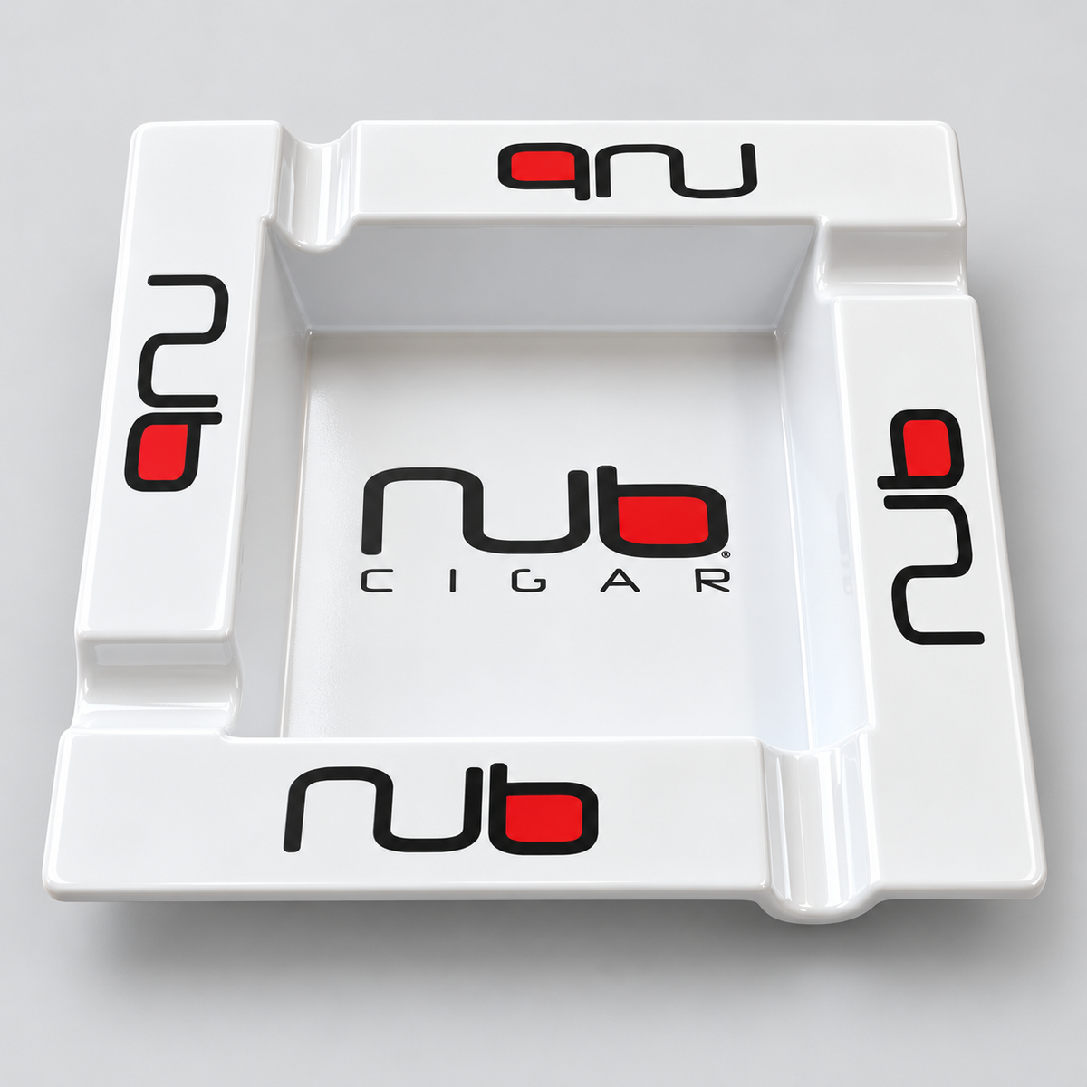 A white ceramic cigar ashtray featuring the 'nub CIGAR' logo printed in black and red on the center and corners, shown on a neutral gray background.