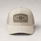 A beige trucker-style baseball cap with a structured front panel and mesh side/back panels. The front features a rectangular olive green patch reading 'GRAN RESERVA LIMITADA 1886 OLIVA CIGAR COMPANY.