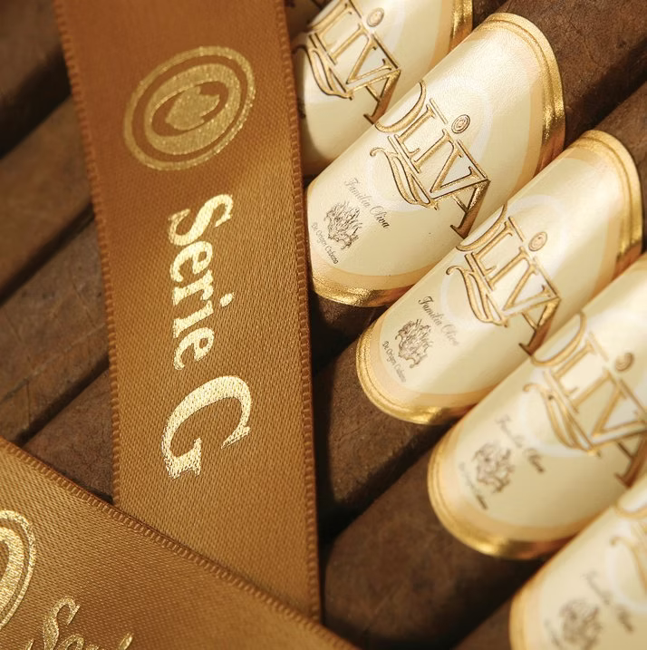 Close-up of luxury jewelry packaging featuring cream-colored cylindrical boxes with gold foil 'Diva' branding, arranged in a brown presentation tray with a matching brown ribbon printed 'Serie G'.