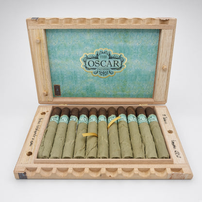 An open wooden presentation box containing 12 rolled cigars, with a turquoise interior lid featuring the 'The Oscar' brand logo. The cigars have dark brown tips and light green bodies with turquoise bands.