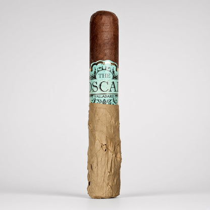 A single cigar standing upright on a light gray background. The cigar has a dark brown wrapper top, a textured tan paper body, and a paper band with teal and black lettering that reads 'THE OSCAR' and 'PALLADAREST'.