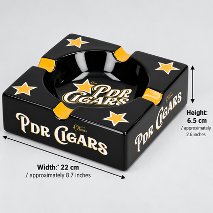 Black PDR Cigars square ashtray with gold lettering and star details, shown with dimension arrows and text indicating width 22 cm and height 6.5 cm on a light gray background.