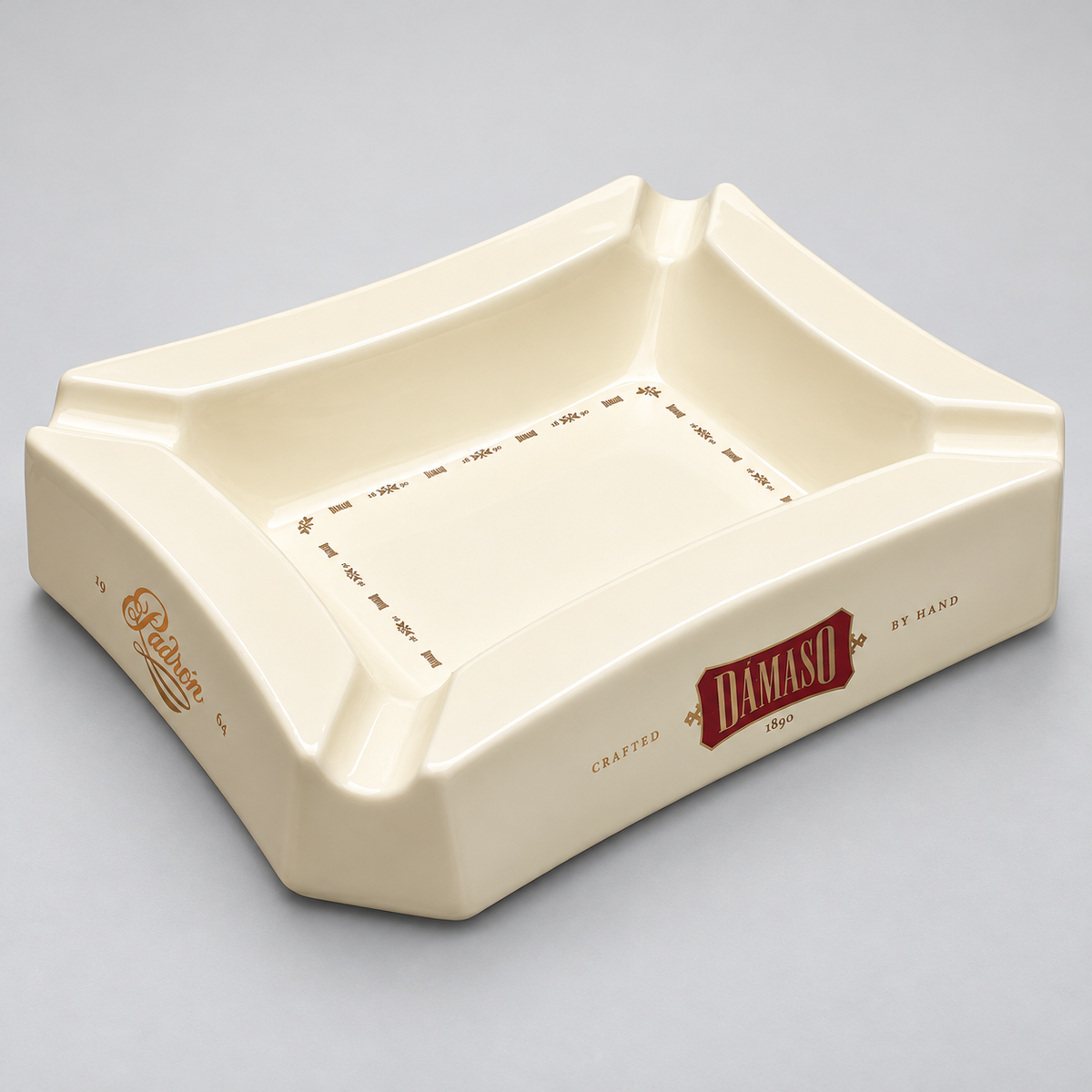 An off-white ceramic square ashtray with four corners, featuring embossed brand names 'Hudson' and 'DAMASO' with a red accent label, set against a neutral gray background.