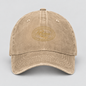 A washed beige baseball cap with a tonal gold embroidered oval logo on the front, photographed against a neutral light gray background.