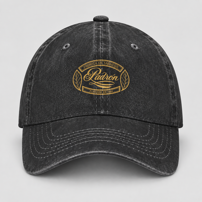 A black washed baseball cap with a gold embroidered oval logo on the front that reads 'Madron Family Farm' and 'Falcone & Smith'.