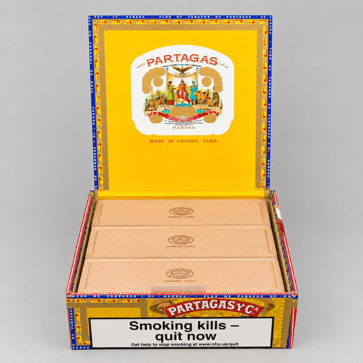 An open box of Partagas cigars on a neutral gray background, showing the yellow interior lid with the Partagas logo and the natural wood cigar leaves inside.