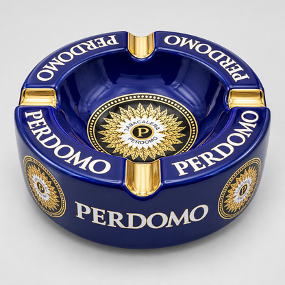 A glossy dark blue ceramic ashtray with gold and white details, featuring the brand name 'PERDOMO' printed repeatedly around the rim and a circular gold emblem in the center.