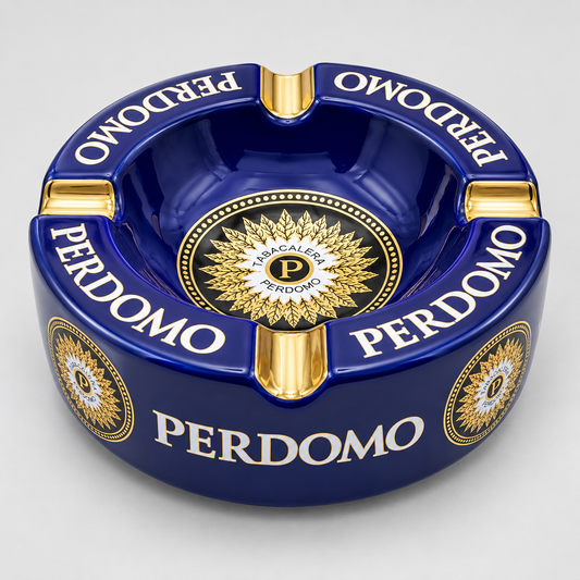 A glossy dark blue ceramic ashtray with gold and white details, featuring the brand name 'PERDOMO' printed repeatedly around the rim and a circular gold emblem in the center.