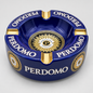 A glossy dark blue ceramic ashtray with gold and white details, featuring the brand name 'PERDOMO' printed repeatedly around the rim and a circular gold emblem in the center.