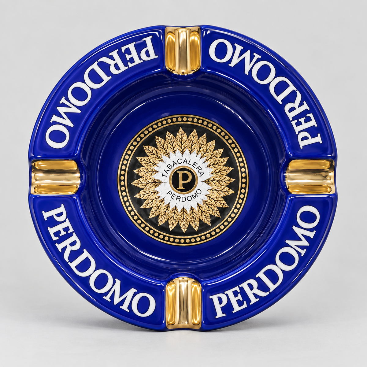 A round blue and gold ceramic ashtray featuring the Italian phrase 'PERDOMO' in white lettering and a central gold crest with a 'P' inside a circle reading 'LA ACACALEPE PERDOMO'.