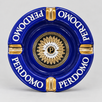 A round blue and gold ceramic ashtray featuring the Italian phrase 'PERDOMO' in white lettering and a central gold crest with a 'P' inside a circle reading 'LA ACACALEPE PERDOMO'.