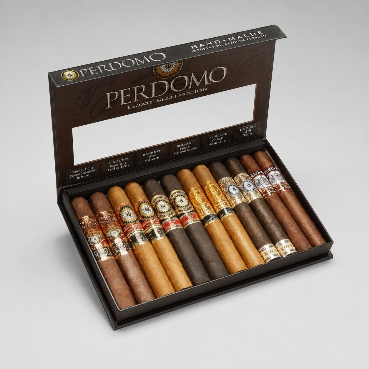 An open Perdomo cigar gift box displaying a selection of various Perdomo hand-rolled cigars in shades of brown, tan, and dark brown, set against a neutral light gray background.