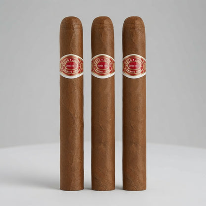 Three brown cigars standing upright side by side on a light gray surface against a light gray background. Each cigar has a red and white band with the text 'MILANO PREMIUM CIGARS' and 'Santa Fe, N.