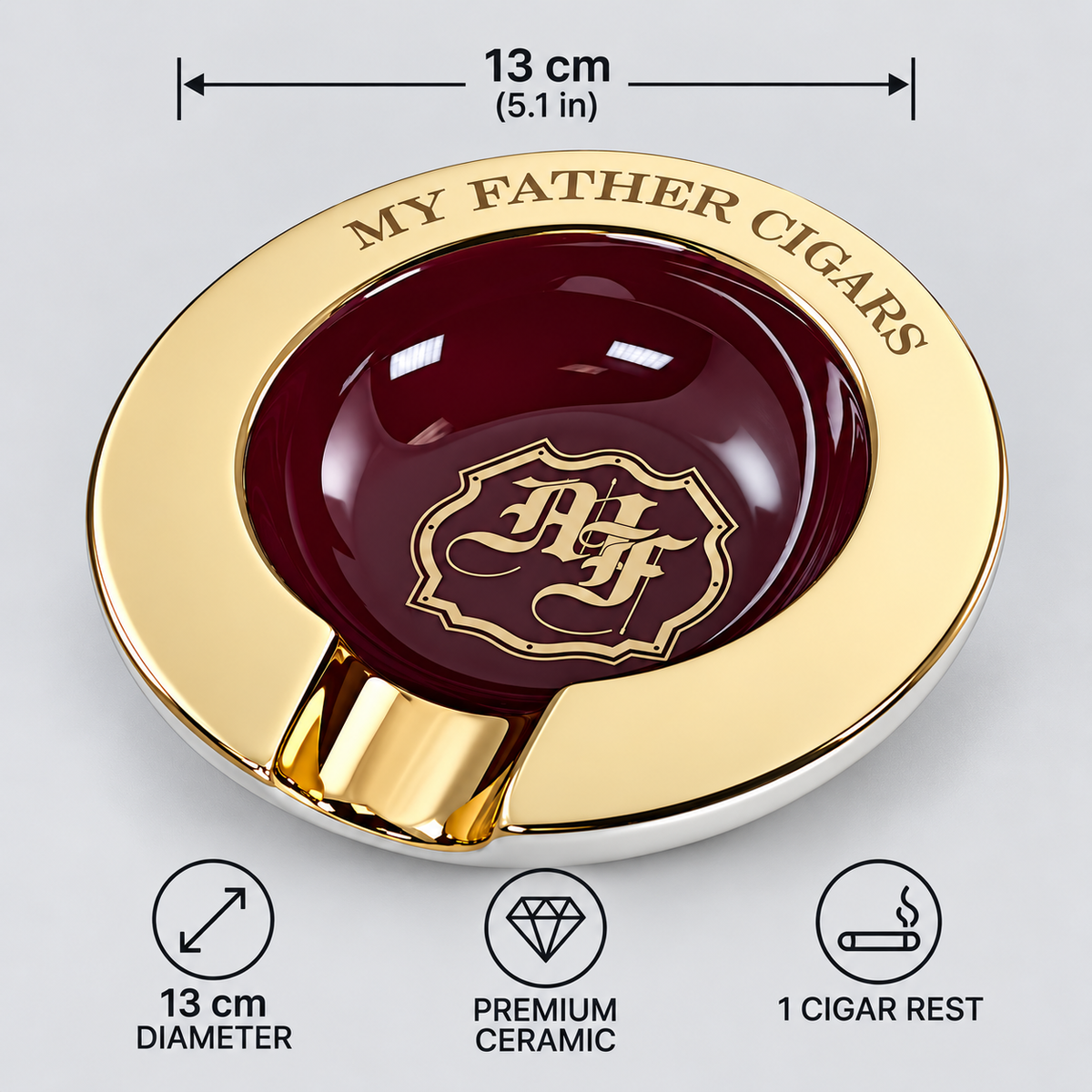 A round cigar ashtray with a polished gold outer rim and a glossy dark red center, shown on a light gray background with measurement and feature callouts. The rim reads 'MY FATHER CIGARS,' and the center has a decorative crest with the letters 'AF.