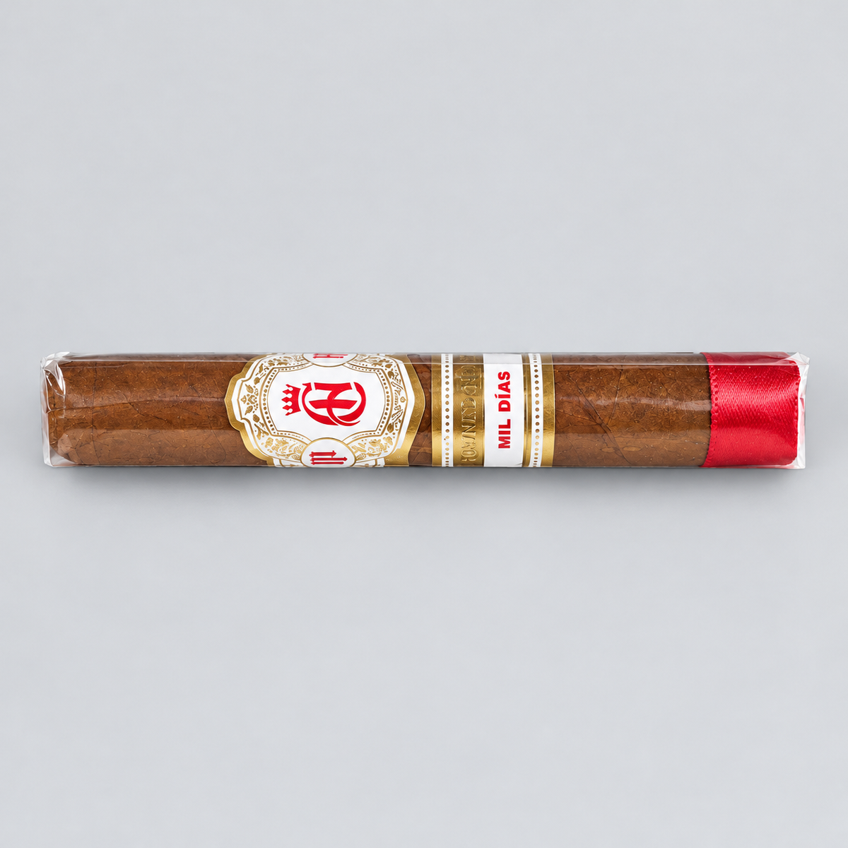 A single cigar in clear plastic wrapping, featuring a white and gold band with red details and a red ribbon tip, photographed horizontally against a solid light gray background.