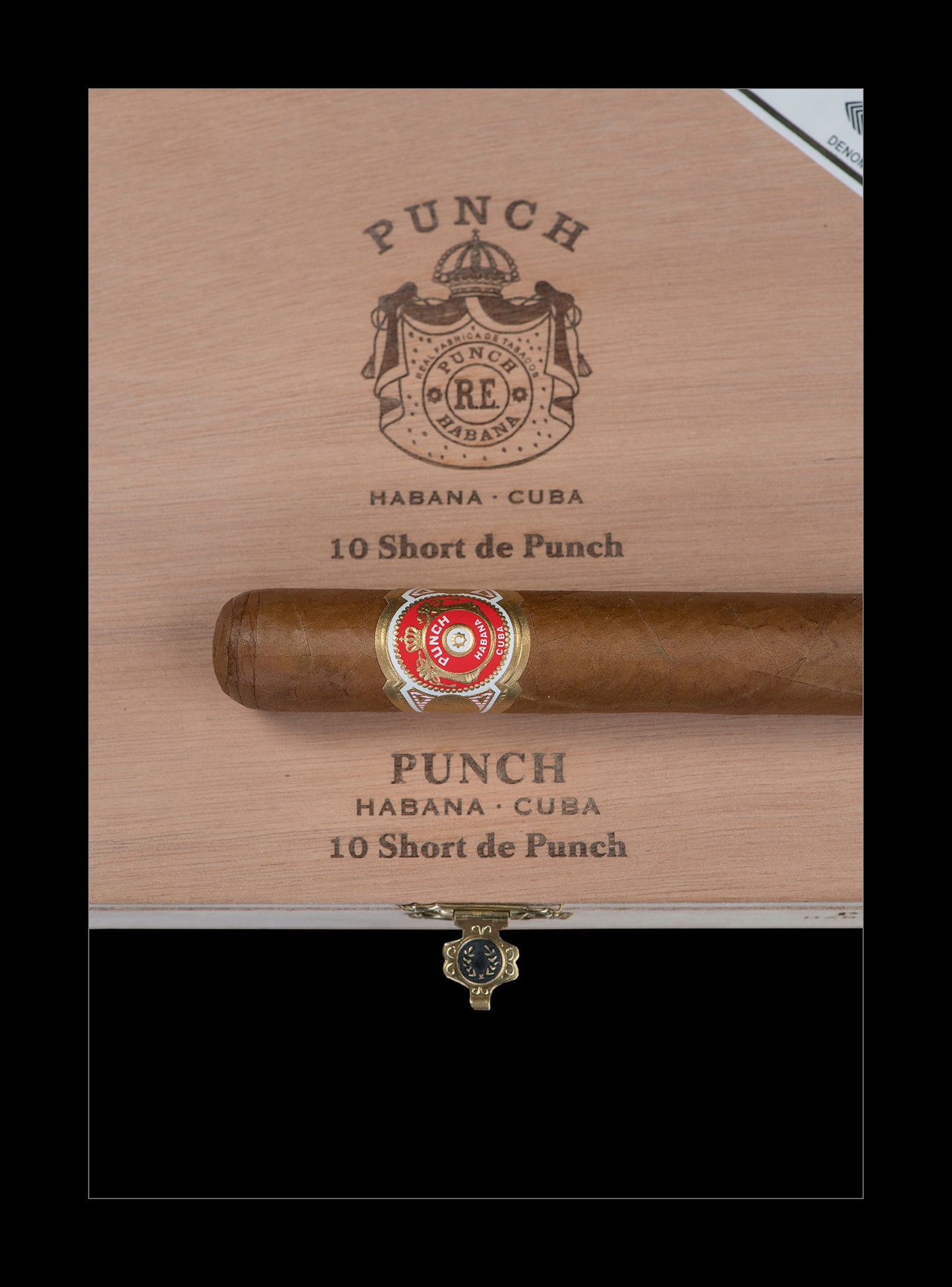A single cigar resting horizontally on a branded wooden box lid. The cigar has a brown body with a red, gold, and white band, and the box is light tan wood with black printed text reading 'PUNCH HABANA - CUBA 10 Short de Punch.