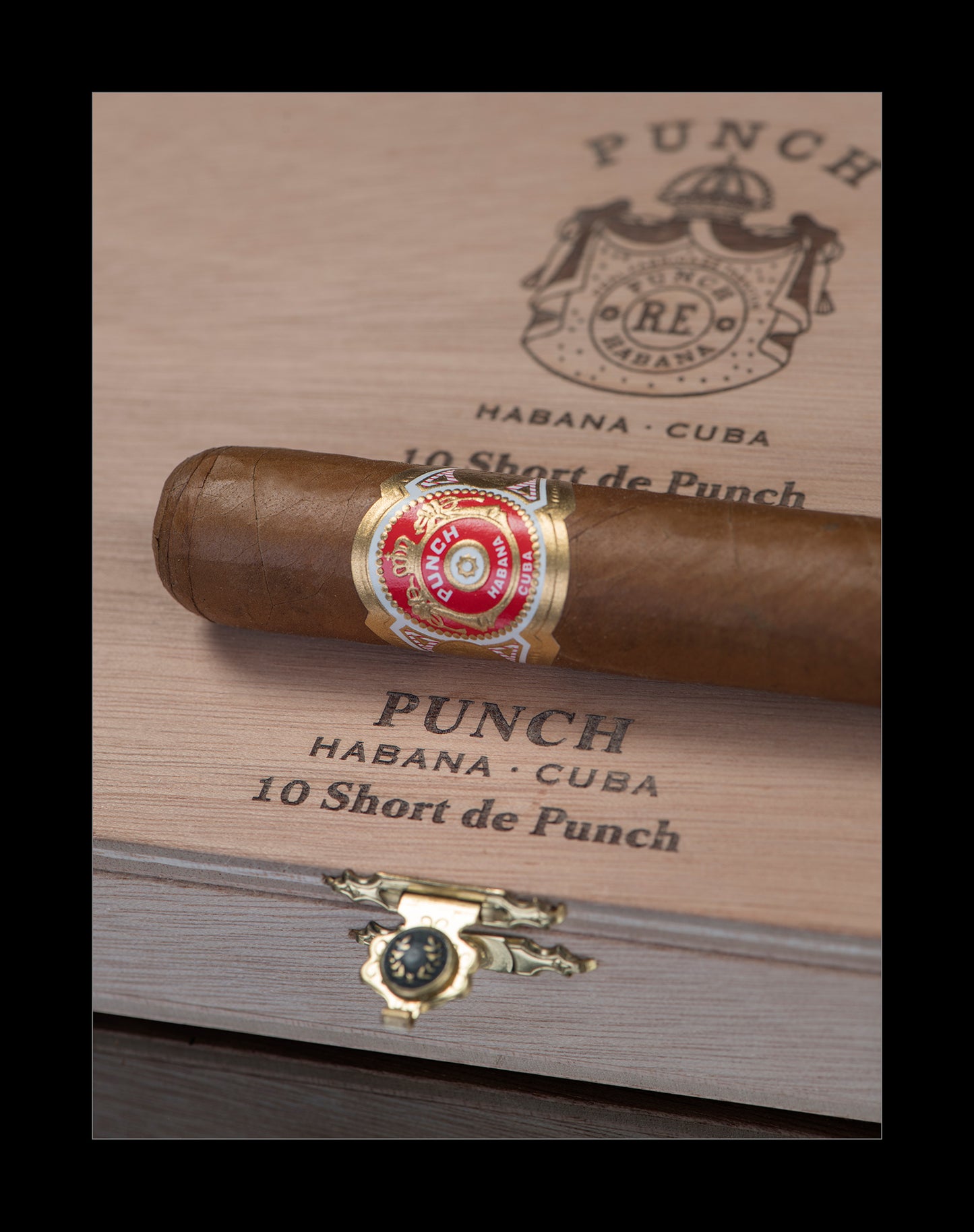 A single cigar resting diagonally across a branded wooden box lid. The cigar has a brown wrapper and a red-and-gold band reading 'Punch Habana - Cuba 10 Short de Punch.