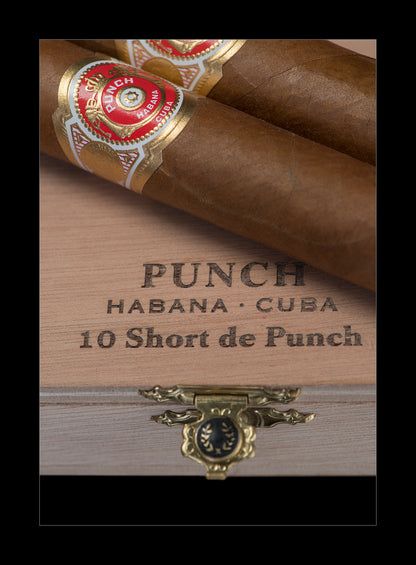 Two brown cigars with red and gold bands resting on a wooden cigar box engraved with 'PUNCH HABANA • CUBA 10 Short de Punch'.